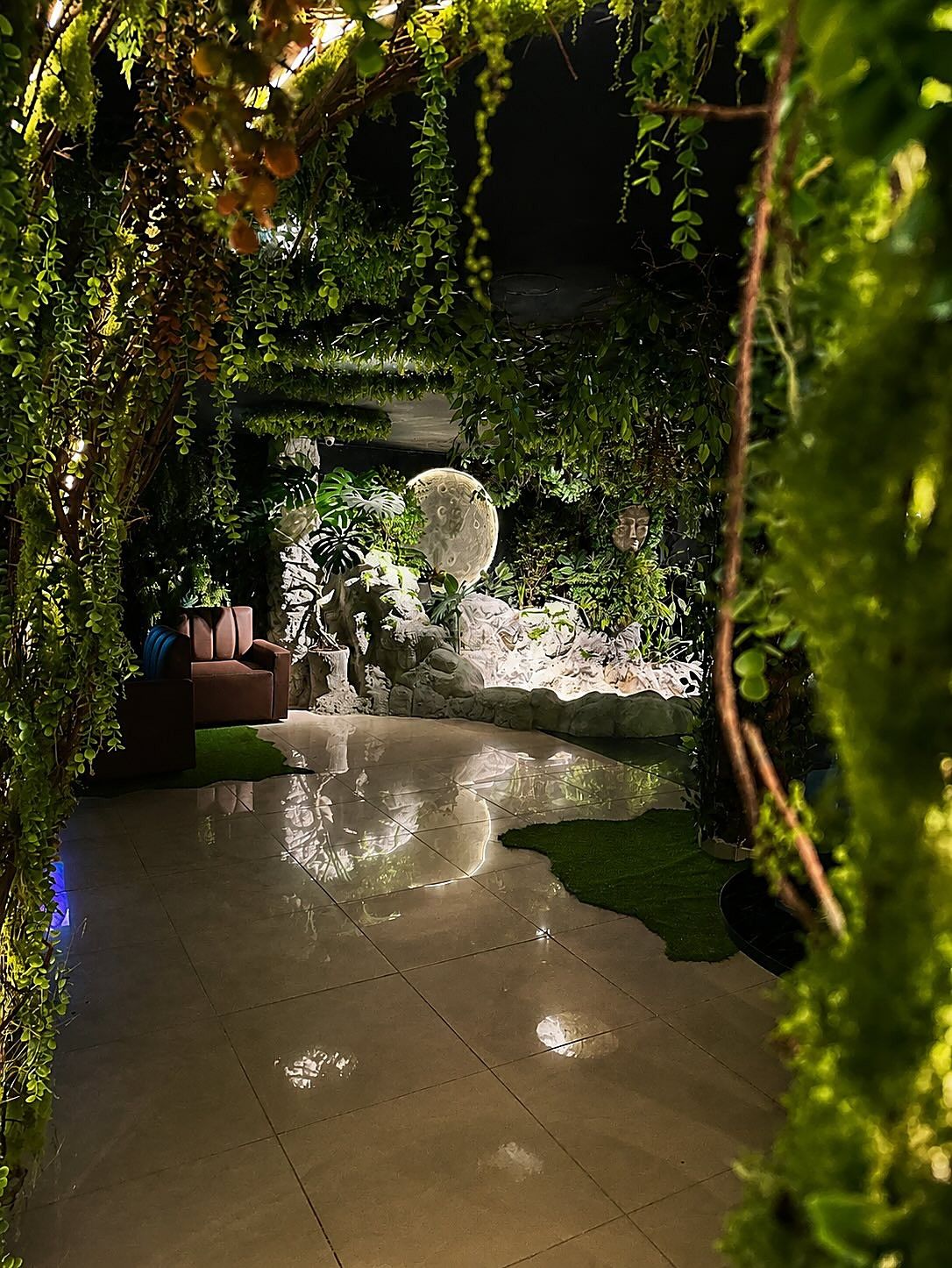 El salón de Selva Negra de noche, con la fuente y la luna al fondo, entre lianas y plantas